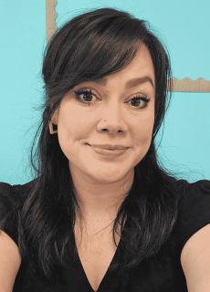 Professional headshot of a Springs Charter Schools staff member smiling in front of a teal classroom bulletin board.