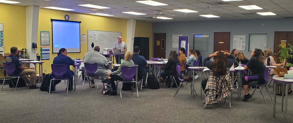 Staff attending Crisis Prevention Institute training in room with gray carpet, light yellow walls, and purple chairs