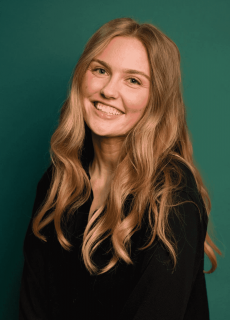 Professional headshot of a smiling woman with long blonde hair wearing a black top against a green background.