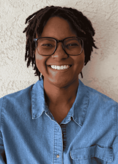 Smiling employee wearing glasses and a denim shirt against a light background.