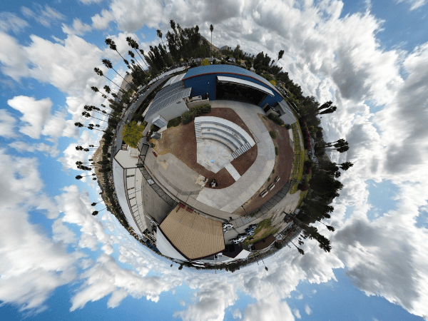 360-degree panoramic “tiny planet” view of a Springs Charter Schools campus, featuring an outdoor amphitheater, buildings, and palm trees under a cloudy sky.
