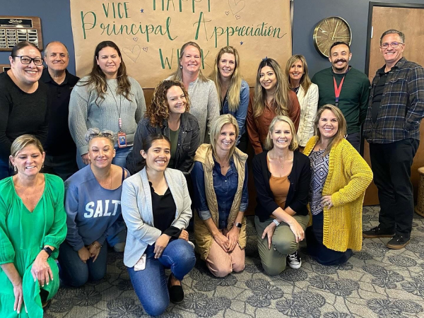 A group of staff members smile together in front of a handmade sign that reads “Happy Vice Principal Appreciation Week.”