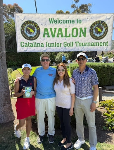 A young golfer stands with three adults under a banner reading “Welcome to Avalon – Catalina Junior Golf Tournament,” smiling and holding a plaque.