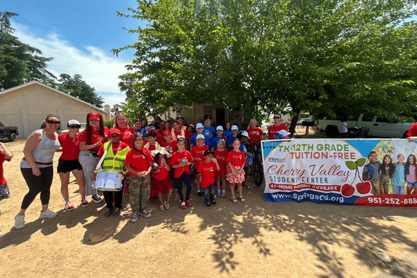 Group of students, staff, and families from Cherry Valley Student Center wearing red shirts, posing by a Springs Charter Schools banner under a tree.
