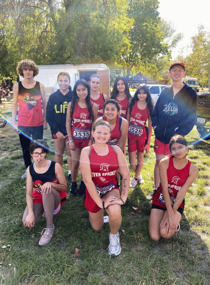 A group of students in red cross country uniforms posing together outdoors at a meet.