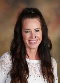 A professional studio portrait of a Springs Charter Schools staff member wearing a white blouse and smiling confidently. The background and polished presentation reflect the professionalism and welcoming nature of Springs educators and staff.