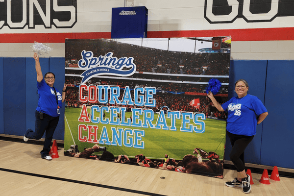 Staff members posing with a Springs Charter Schools banner that reads “Courage Accelerates Change.”