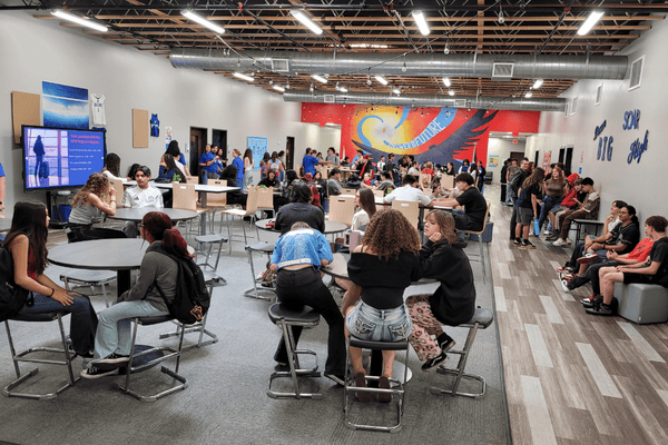 Students socializing and working in a school common area with colorful wall art.