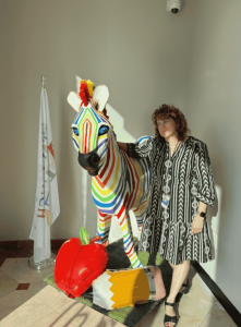 Completed rainbow zebra sculpture with a teacher standing beside it, displayed with a large apple and pencil decoration.