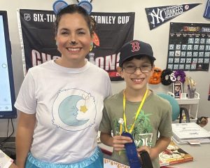 Springs Charter Schools student holding a blue ribbon stands next to a smiling teacher dressed in a fun costume during a classroom spelling bee celebration.