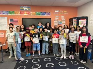 A group of Springs Charter Schools students stand together in a classroom holding spelling bee numbers and ribbons.
