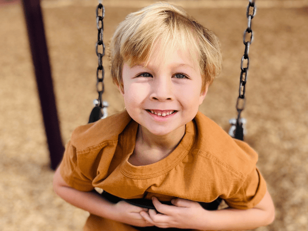 Springs Charter Schools student smiling while sitting on a swing outdoors.