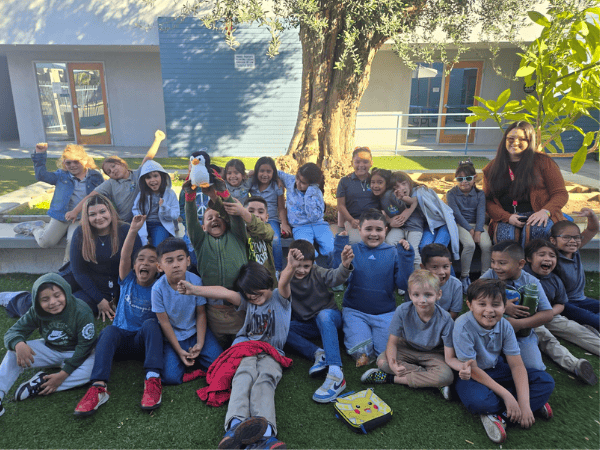 Springs Charter Schools students and teachers smiling together outdoors while sitting under a tree.