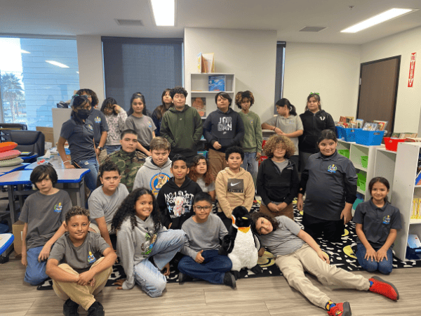 Springs Charter Schools students pose together in a classroom with bookshelves and learning materials in the background.