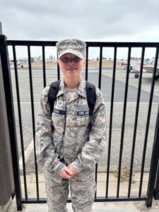 Student wearing a Civil Air Patrol uniform standing near an airfield with small aircraft in the background.