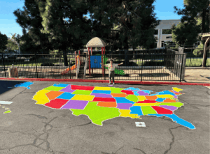 A colorful painted map of the United States displayed on the pavement at a Springs student center playground.