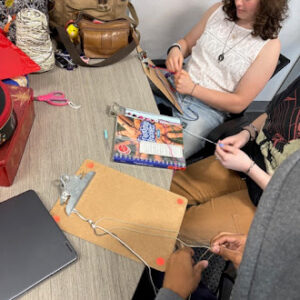 Students working together at a table making bracelets during a hands-on craft workshop.