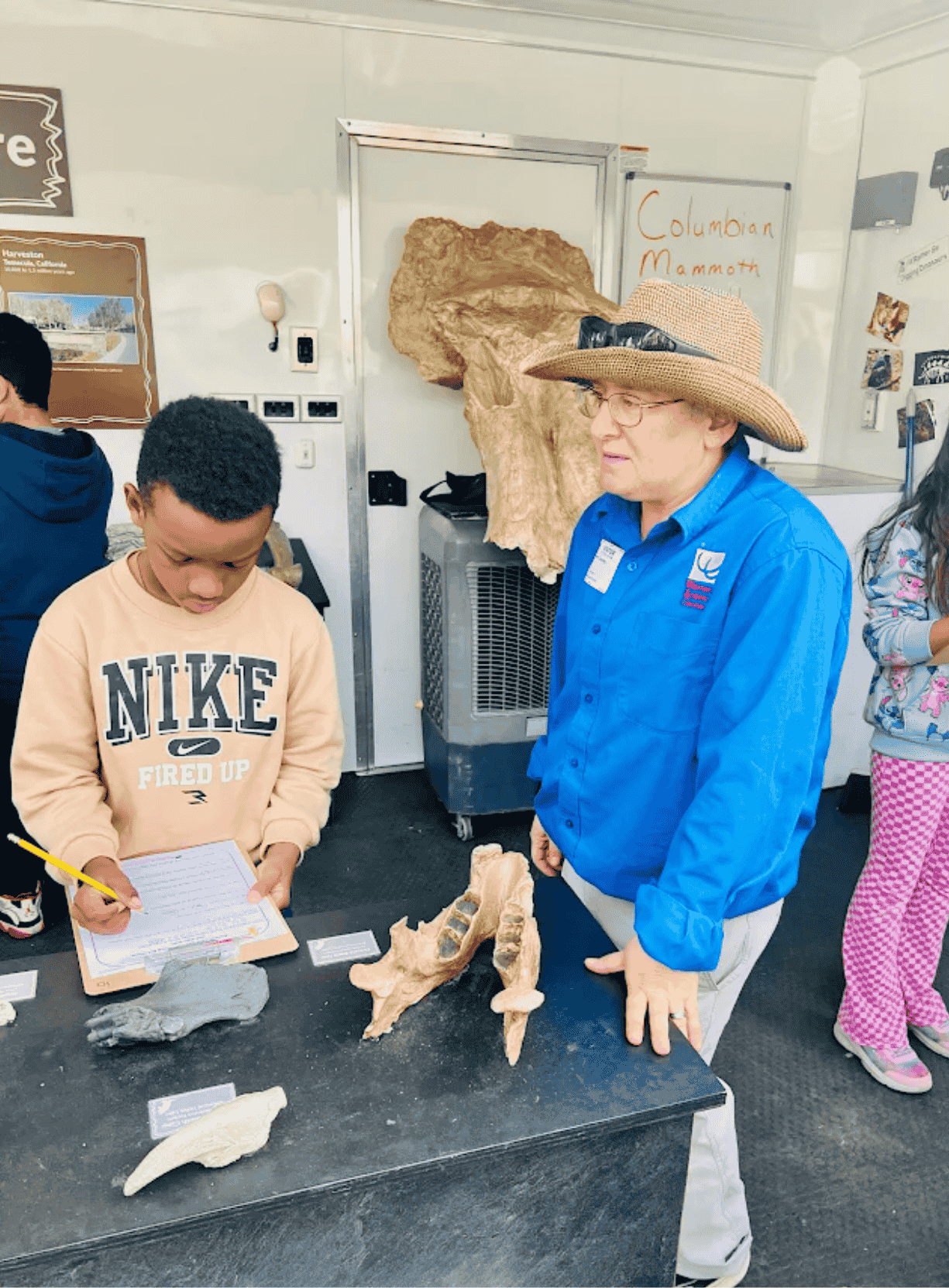 Students gathered around a large mammoth fossil display during a mobile science lab presentation.