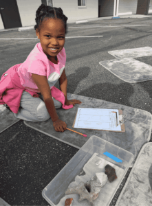 Student sitting outdoors with fossil samples and a worksheet during a hands-on science investigation.