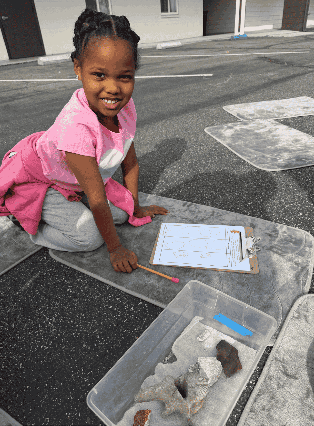 Student sitting outdoors with fossil samples and a worksheet during a hands-on science investigation.
