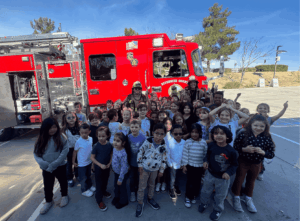 Group of students posing with firefighters in front of a fire truck on campus.
