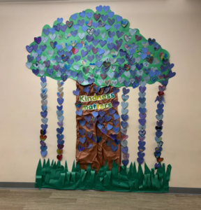 Large tree mural made of blue and green paper hearts with the words “Kindness matters” displayed on a school wall.