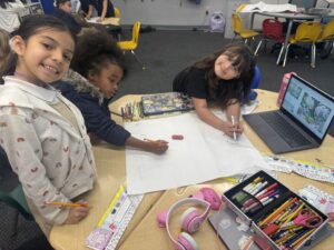 Group of students gathered around a table working on a shared drawing with a laptop nearby.