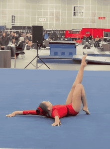 Student in red leotard performing a gymnastics routine on a floor mat.