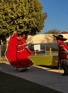 Two students performing a traditional dance outdoors, one in a red dress and one in a sombrero.
