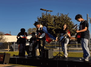 Group of students playing instruments on a small outdoor stage during a performance.