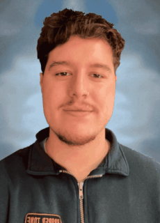 Man with short dark hair and light facial hair wearing a zip-up jacket against a blue background.