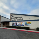 Exterior view of River Springs Charter School building with signage and banners displayed along the front wall.
