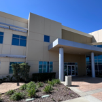 Exterior view of Exploration Student Center building with modern design, glass entrance, and landscaped walkway under a clear blue sky.