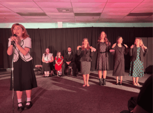 Students performing on stage during a school theater production under colorful stage lighting.