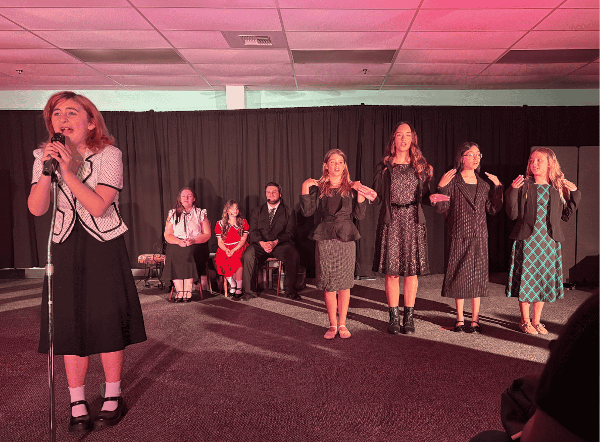 Students performing on stage during a school theater production under colorful stage lighting.