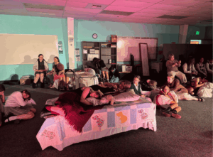 Students acting in a dramatic theater scene with stage props and lighting during a school performance.