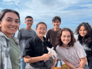 High school students smiling together during a coastal field trip and outdoor learning experience.