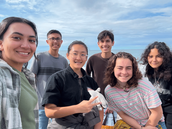 High school students smiling together during a coastal field trip and outdoor learning experience.