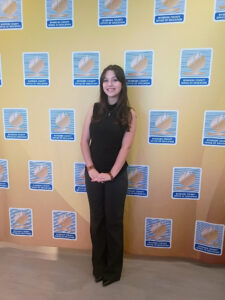 Student posing in front of a Riverside County Office of Education backdrop during a formal academic or recognition event.