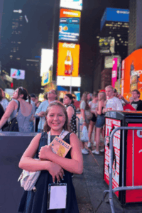 Student smiling in Times Square while holding a theater playbill during an educational travel experience.