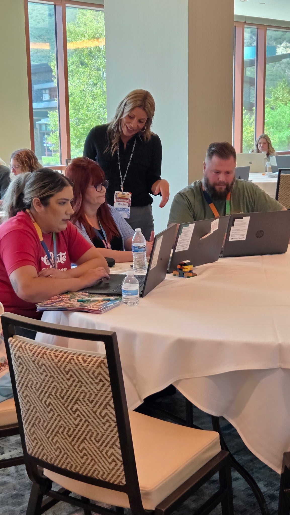 A instructor assisting staff members working on laptops around a round table during an IGNITE professional development workshop.