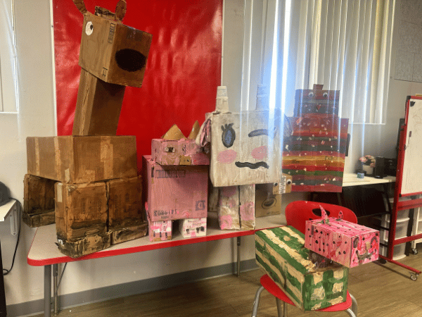 A collection of colorful cardboard sculptures and animal figures created by students displayed on tables in a classroom.