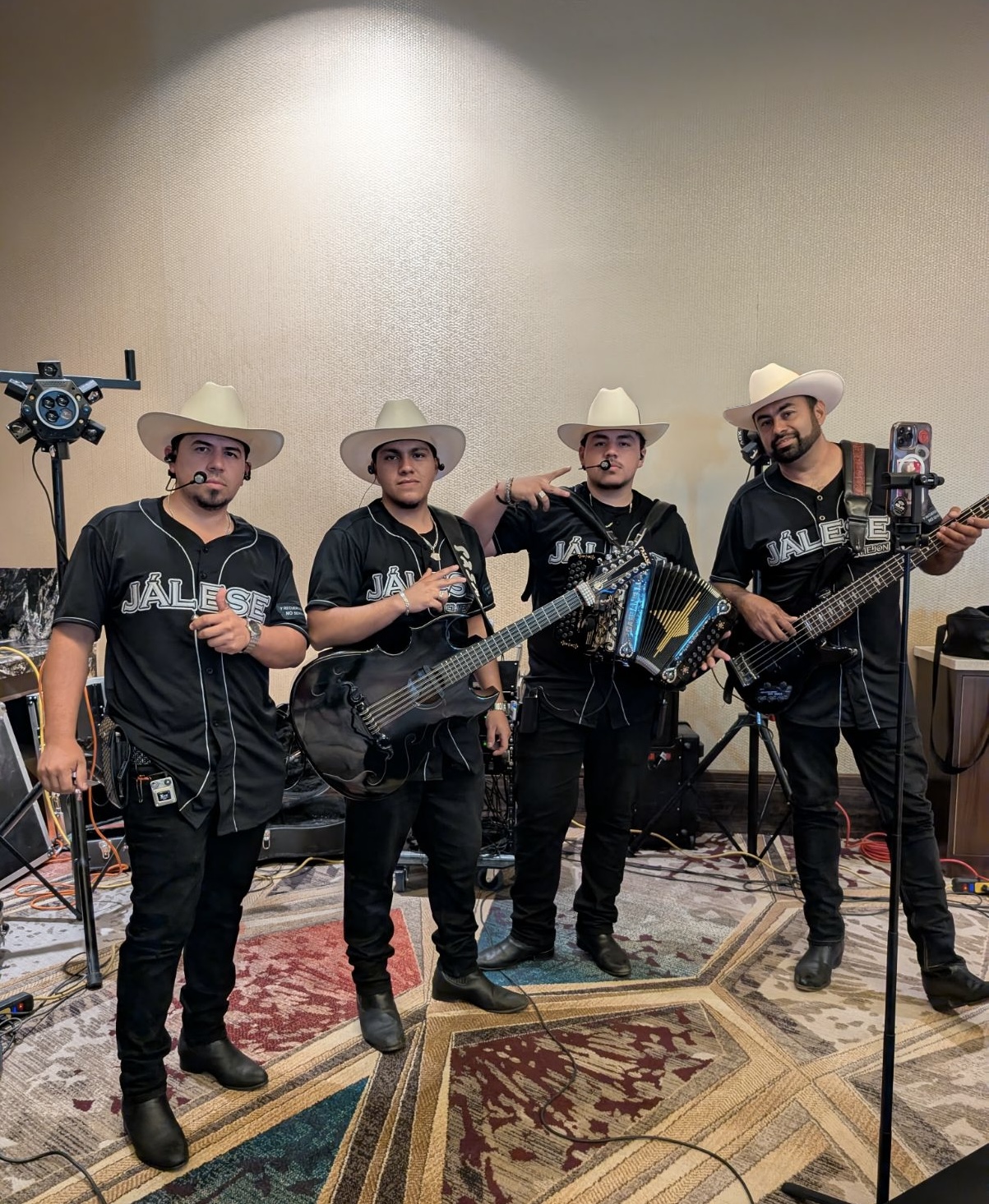 Four River Valley Academy students matching in black band shirts and cowboy hats posing indoors with an accordion and guitars.