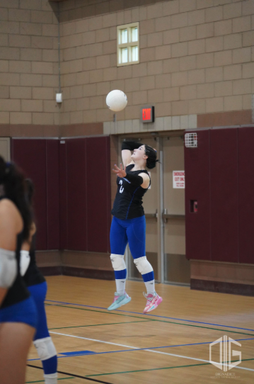 A high school student leaping into the air to serve a volleyball during an indoor match in a gymnasium.