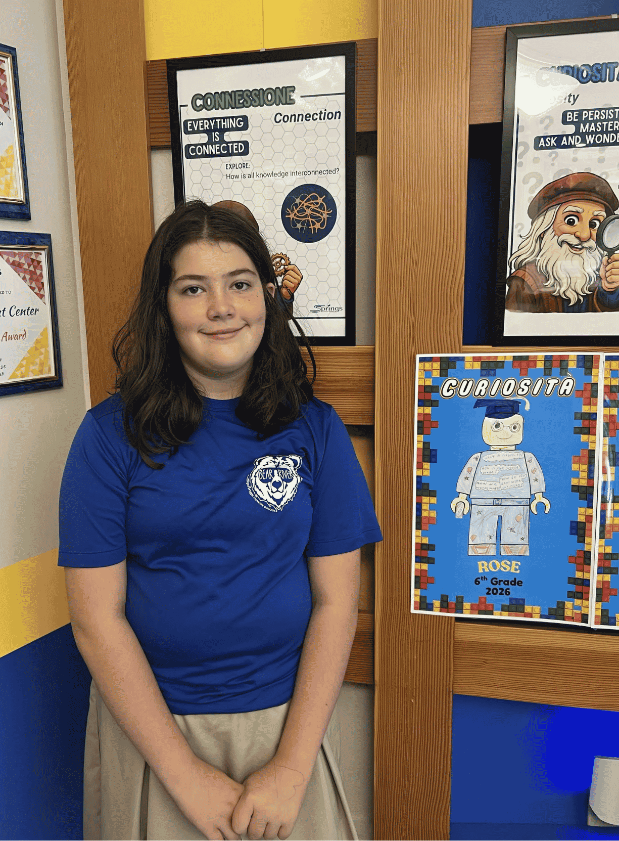 A student wearing a Bear River school shirt posing beside a poster display in a classroom hallway.