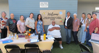 School leaders and administrators posing together outdoors in front of a welcome banner at Palm Academy Student Center